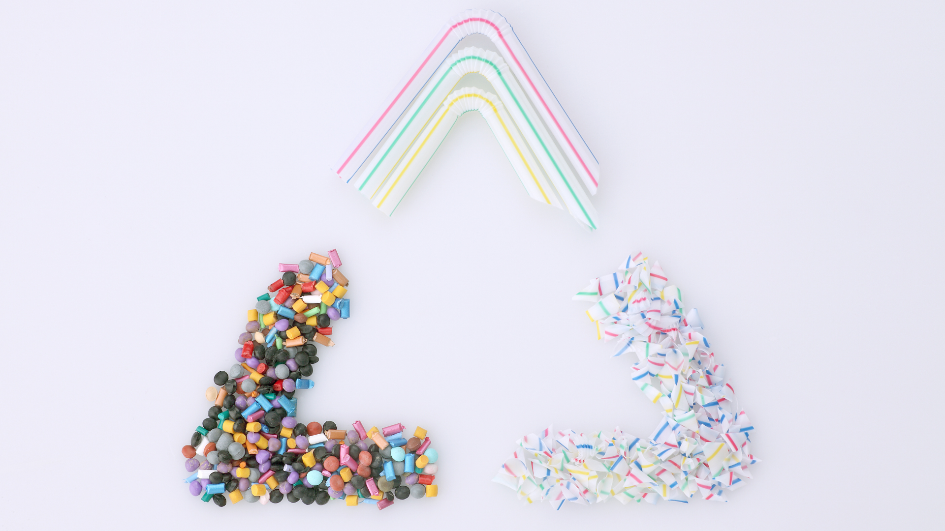 Plastic recycling symbol made from colorful microplastic pellets, plastic straws, and shredded plastic.