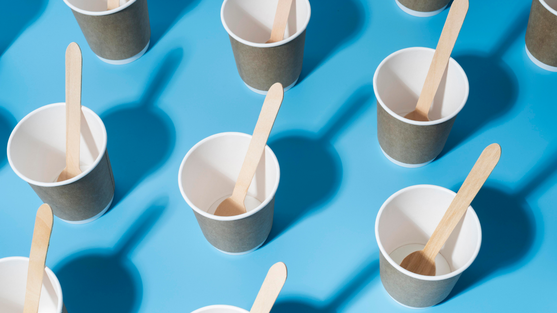 Compostable paper cups with wooden stirrers on a blue background, showcasing plant-based alternatives to single-use plastic cups.